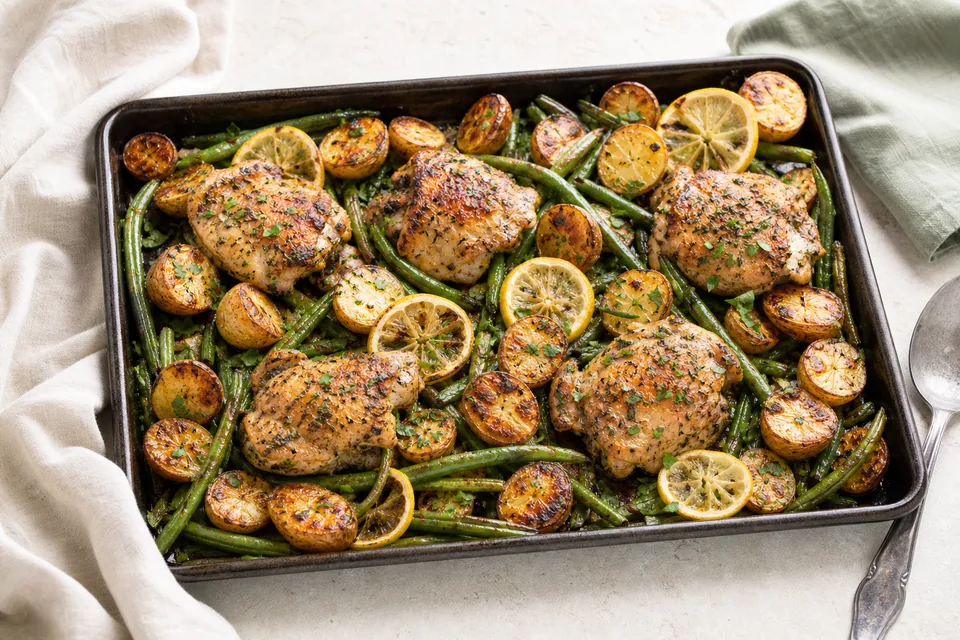 Finished sheet pan of golden lemon herb chicken thighs, browned potatoes, green beans, lemon, and parsley
